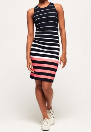 Femme portant une robe sans manches, longueur genou, avec des rayures horizontales bleu marine, blanches et roses et des baskets blanches avec des motifs d'étoiles.