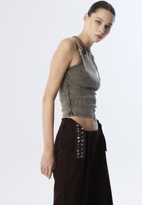 Top in canotta grigio a coste con spalline. Pantaloni a gamba larga color marrone scuro con bottoni a pressione argentati sul lato sinistro.