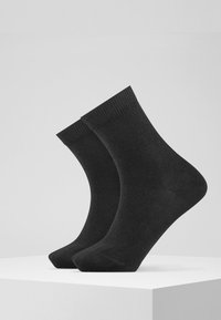 Calcetines de algodón negros con puños acanalados y textura suave, exhibidos sobre un pedestal blanco contra un fondo gris.