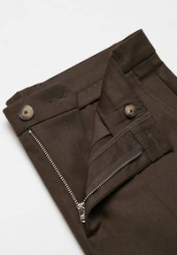 Ceinture d'un pantalon marron avec une fermeture éclair métallique partiellement ouverte et deux boutons ronds sur fond blanc.