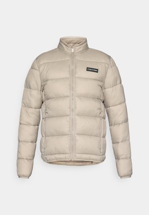 Casaco puffer em bege, acolchoado, com fecho éclair frontal completo, dois bolsos laterais com fecho, gola alta e logótipo Calvin Klein no peito.