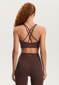 Rjava športna modrček z prekrižanimi naramnicami in logotipom, kombiniran z visokim pasom rjavih legic. Gladek tekstura in minimalističen dizajn.