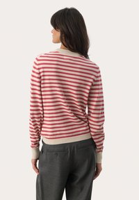 Gestreifter Pullover in Rot und Creme, gerippte Bündchen und Saum, weicher Stoff, lockere Passform, runder Ausschnitt, getragen zu grauen maßgeschneiderten Hosen.