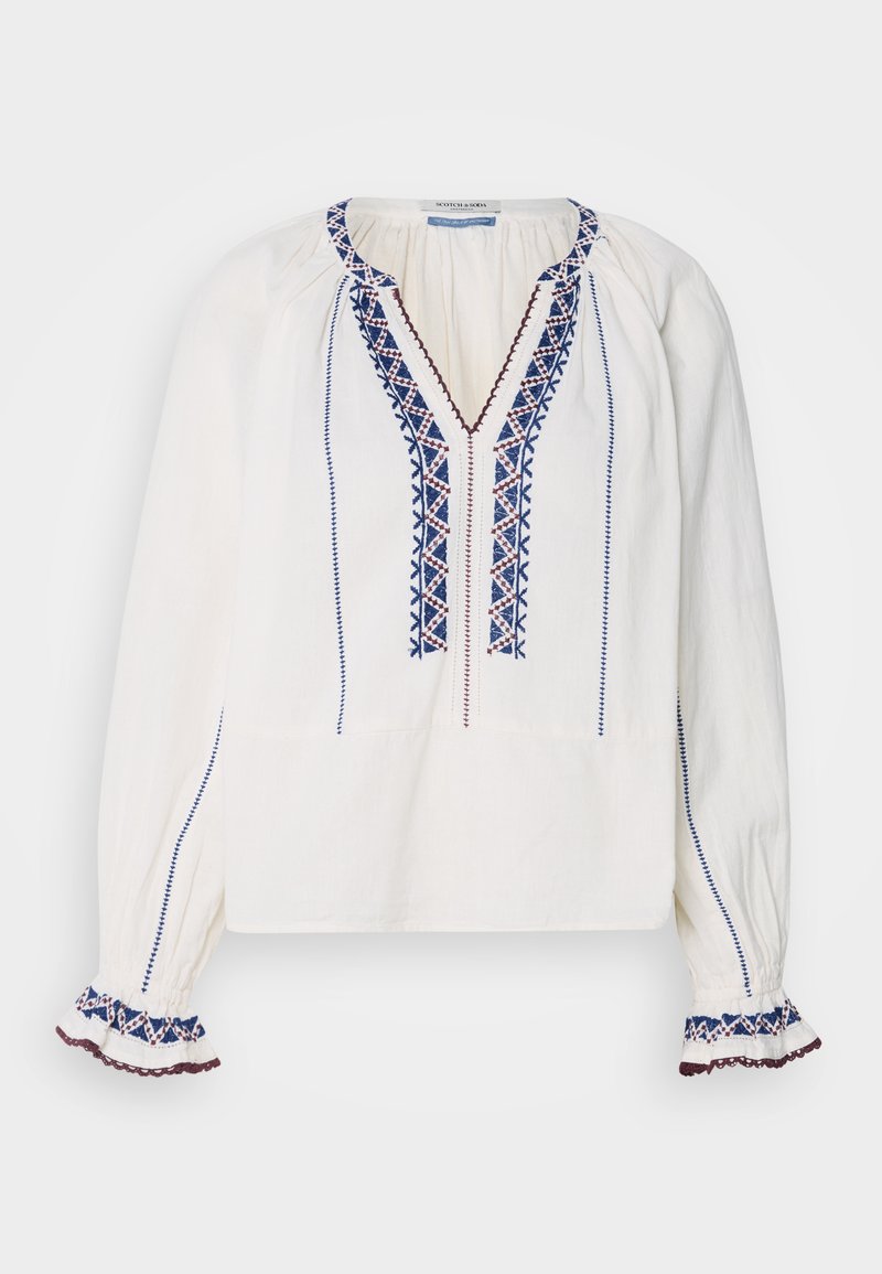 Blouse blanche à manches longues avec un décolleté en V, ornée de broderies bleues et bordeaux le long de la patte de boutonnage et des poignets. Tissu doux et léger.