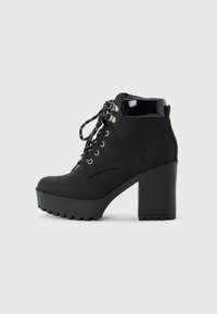 Bottine en cuir noir à lacets avec un talon haut épais, semelle à plateforme, œillets en métal et détail de col rembourré brillant, vue de côté sur fond blanc.