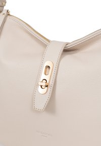 Beige nahkalaukku, jossa on kultainen vetoketju, litteä hihna ja erottuva kultainen kiinnitys, jossa on keskellä leikattu yksityiskohta.