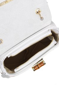 Interno di una borsa in pelle bianca con due cerniere dorate, foderato in beige e un accento in legno sulla chiusura. Esterno in suede texture.