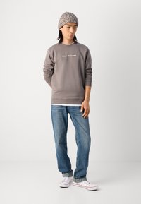 Pelēks sporta krekls ar uzrakstu "Mare O'Polo DENIM", zili džinsi un balti kedas. Akcentēts ar teksturētu adītu cepuri.