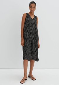 Schwarzes ärmelloses Kleid mit V-Ausschnitt, das weiße Punkte, eine lockere Passform und eine midi-lange mit einem rüschengesäumten Saum aufweist.