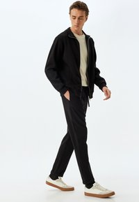 Sort zip-up sweatshirt og matchende joggers, parret med hvide sneakers. Glat stof med ribbede manchetter og et simpelt design.