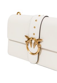Bolso blanco con un cierre dorado que presenta dos diseños de pájaros y tachuelas decorativas a lo largo de la correa, resaltando su diseño elegante y estiloso.