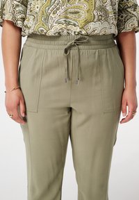 Pantalon de jogging vert olive clair avec une taille élastique, un cordon de serrage ajustable et deux poches avant ; texture lisse avec un minimum de détails.