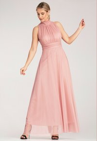 Różowa sukienka na halter wykonaną z przezroczystego materiału, z plisami na górze, dopasowanym pasem i zwiewną spódnicą. Czarne sandały na obcasie.