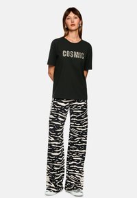 Black t-shirt with "COSMIC" graphic in a textured print, paired with wide-leg trousers in a beige and black animal print design.