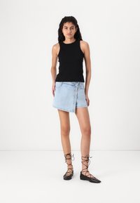 Black sleeveless top paired with a light blue denim mini skirt featuring a button closure and studded accents, complemented by black lace-up flats.