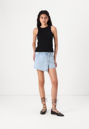 Top sans manches noir associé à une mini-jupe en denim bleu clair avec une fermeture à bouton et des accents cloutés, complété par des ballerines noires à lacets.