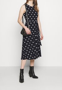 Námořnické šaty s puntíky, s těsným korzetem a rozšířenou sukní; doplněné malou černou kabelkou přes rameno a černými botami na podpatku do kotníku.