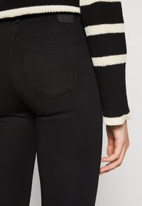 Czarne elastyczne dżinsy o gładkiej fakturze, z klasycznym wzorem tylnej kieszeni i małą metką marki naszytą blisko pasa.