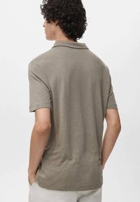 Polo tričko s krátkým rukávem v světle olivové barvě, vyrobeno z měkké látky, s klasickým límečkem a přímým lemem. Minimální design, bez ozdob.