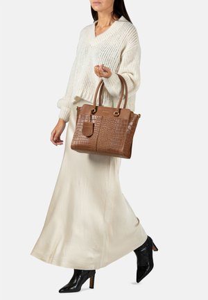 Sac à main en cuir texturé marron avec motif crocodile et poignées doubles. Accompagné d'un pull crème et d'une jupe en lin.