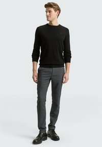 Black knit sweater with round neckline, paired with gray textured trousers and black lace-up shoes. Simple and modern design.