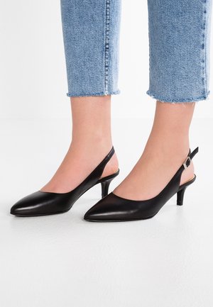 Sorte læder slingback kitten heels båret med lyseblå, croppede jeans med frynset kant på hvidt gulv.