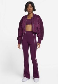 Ensemble sportif violet comprenant une veste bomber courte avec des manches texturées, un soutien-gorge de sport assorti et un pantalon de jogging évasé avec des accents blancs.