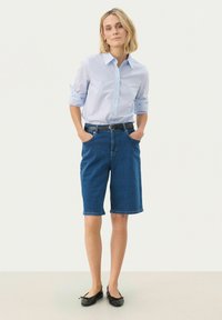 Gaiši zils uzvalka krekls, denima berbuša šorti un melni plakanie apavi. Šortiem ir sānu kabatas. Materiāls ir gluds; krekls ar sarullētām piedurknēm.