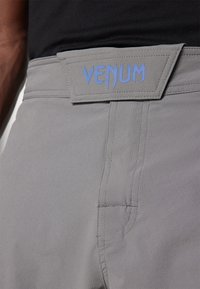 Šedé športové šortky s textúrovanou tkaninou, modrou logom VENUM na páse a plochými švami pre pohodlie a flexibilitu.