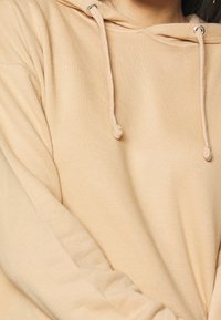 Beige hoodie met een zachte textuur, voorzien van een capuchon met trekkoord, metalen oogjes en lange mouwen. Eenvoudig ontwerp, geen zichtbare patronen.