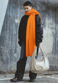 Geacă neagră din piele, eșarfă portocalie texturată, blugi închiși, pantofi maro și o geantă hobo bej deschis cu litere aurii. Fundal neutru.