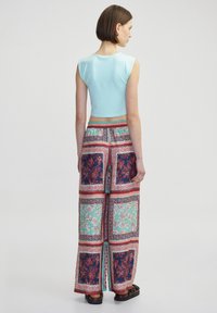 Top corto blu chiaro abbinato a pantaloni a gamba larga con una stampa floreale e geometrica in rosso, teal e blu navy, tessuto testurizzato.