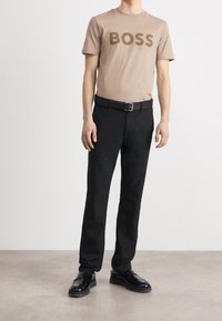 Beige T-shirt med "BOSS"-logotyp, svarta byxor, svart bälte och glänsande svarta skor. Mjukt tyg och skräddarsydd passform, minimalistisk design.