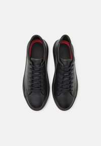 Sneakers neri con tomaia in pelle liscia, punta rotonda e interno rosso a contrasto. Presentano lacci neri piatti e un design minimalista.