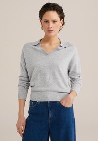 Siv pulover s V-izrezom in ovratnikom, rebrasti manšeti in spodnjim robom, mehak material, v kombinaciji z visokim jeansom.