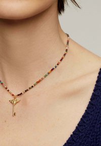 Collar de cuentas multicolores con pequeñas cuentas redondas y un colgante decorativo en forma de llave dorada. La vista en primer plano resalta la textura y los detalles.