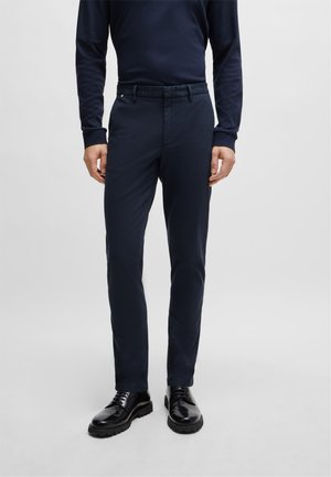 Tummansiniset housut, jotka on valmistettu puuvillasekoitekankaasta, slim fit -muotoilu, jossa on litteä etuosa, vyölenkit ja sileä pinta. Yhdistetty mustiin kenkiin.