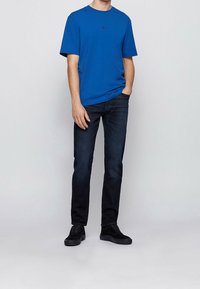 Blå bomullströja med korta ärmar och rund halsringning, tillsammans med mörka denimjeans och svarta sneakers. Minimalistisk design, inga synliga mönster.