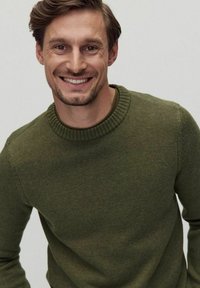 Grön pullovertröja med ribbad rund hals, tillverkad av strukturerad stickad tyg. Har en figursydd silhuett och mjuk yta.