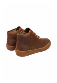 Botas de tobillo de cuero marrón con diseño de cordones y suelas de goma texturizadas, mostradas desde atrás y de lado sobre un fondo blanco.