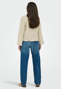 Beige Texturjacke mit weiten Ärmeln, kombiniert mit locker sitzenden blauen Jeans. Das Outfit hat ein kurzes Design und Jeans mit Gesäßtaschen.