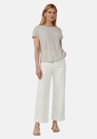 Jasnoszary, dzianinowy top z krótkim rękawem w połączeniu z białymi spodniami o szerokich nogawkach. Modelka nosi beżowe sandały z plecionymi paskami. Prosty, minimalistyczny design.