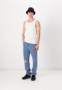 Hvid bomulds tanktop med et lille rødt logo, parret med lyseblå ripped jeans og sorte sneakers. En sort bøttehat fuldender looket.
