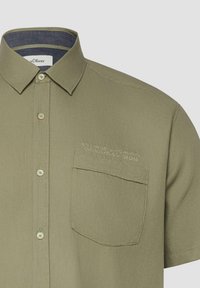 Chemise à manches courtes vert olive avec poche avant et texte brodé au-dessus de la poche indiquant "s.Oliver Genuine Garments."