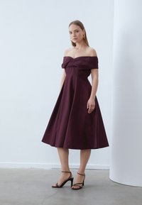 Βουργουνδί φορεμα χωρίς ώμους με εφαρμοστό μπούστο και ρο flowy φούστα. Λεπτός ύφασμα με κόμπο στο στήθος. Μαύρα πέδιλα με λουράκια.