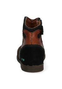 Botín de tobillo de múltiples materiales en marrón y negro, con lados texturizados, una correa de velcro y puntos de acento verdes en el tacón. Cuero suave y tela blanda.