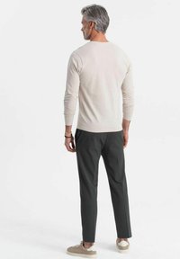 Camisa de punto crema de manga larga combinada con pantalones gris oscuro y zapatillas marrón claro, vista desde la parte de atrás. Silueta elegante con detalles mínimos.