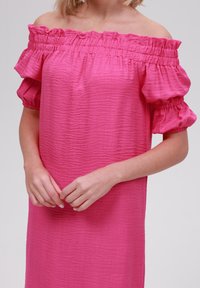 Rosa off-shoulder klänning med volangärmar och texturerat tyg. Designen har en avslappnad passform och elastiska detaljer vid halsringningen.