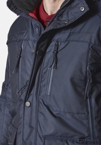 Marineblaue isolierte Jacke mit durchgehendem Reißverschluss, mehreren Taschen und Kordelzüge. Verfügt über einen fleecegefütterten Kragen für zusätzliche Wärme.