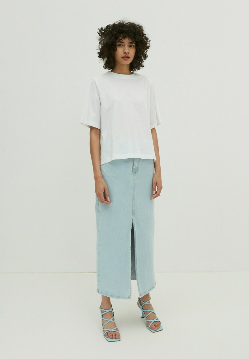 Witte korte mouwen t-shirt gecombineerd met een lichtblauwe denim rok met een split aan de voorkant en een rafelzoom. Blauwe sandaaltjes met hakken maken de look af.